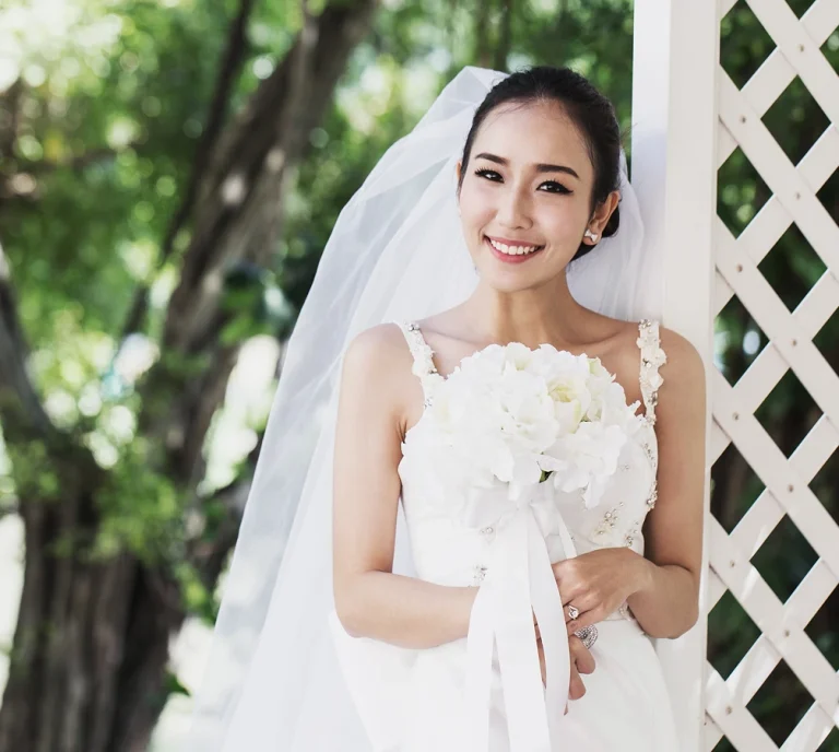 portrait-smiling-young-bride-wearing-wedding-dress-while-holding-bouquet-park